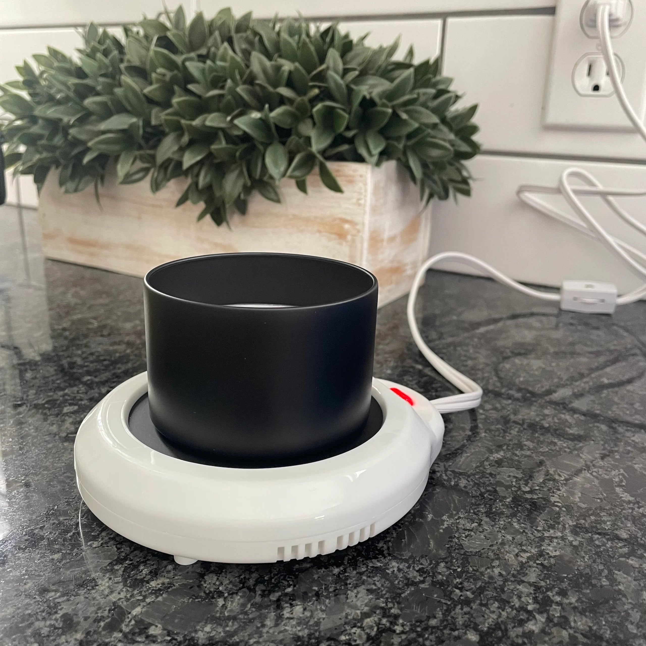 Black mug on a white hot water bottle on a kitchen counter with a plant in the background.