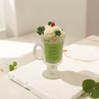 Green milkshake with whipped cream and clover leaves on a white surface